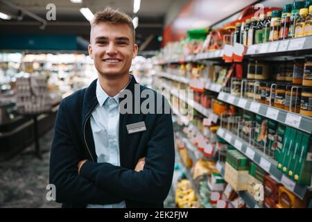 Porträt eines Mannes in Uniform, der mit gekreuzten Armen im Lebensmittelgeschäft steht. Männlicher Arbeiter im Supermarkt. Stockfoto