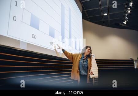 Geschäftsfrau, die auf der Leinwand Gesten macht und während des Seminars eine Präsentation hält. Rednerin bei der Konferenz. Stockfoto