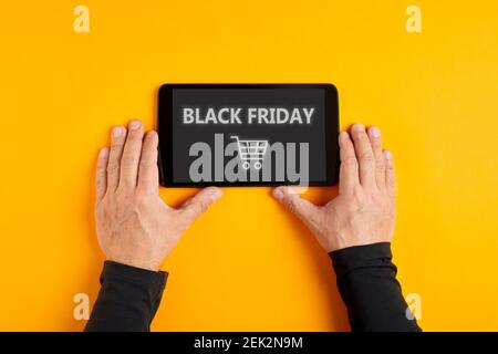 Männliche Hand hält ein digitales Tablet mit dem Wort Black Friday und einem Warenkorb-Symbol auf dem Bildschirm. Black Friday Verkauf und Shopping Mania Konz Stockfoto