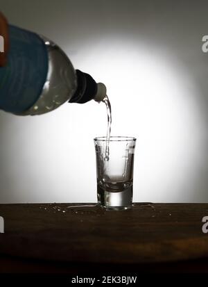 Ein Wasserstrom fließt in ein Glas aus einer Flasche auf einem alten Holztisch als detailreiche Nahaufnahme, transparentes Glas mit Flüssigkeit. Glas übergeben Stockfoto