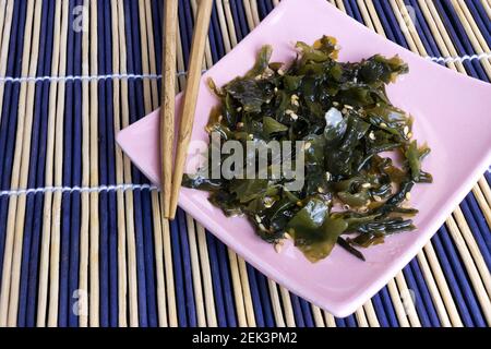 Als nächstes werden getrocknete Wakame-Algen mit Sesamsamen auf einem Teller aufgesetzt Zu Essstäbchen Stockfoto