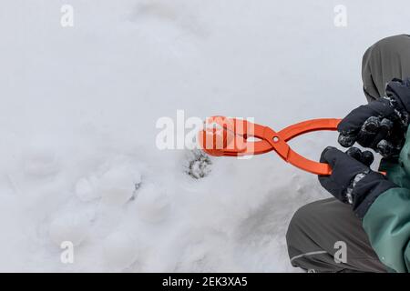 Kind in Skihandschuhen hält Gerät für die Herstellung von Schneebällen Stockfoto