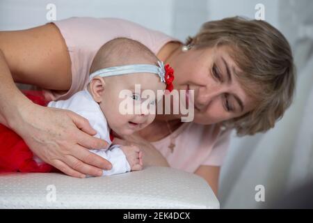Die Großmutter schaut das neugeborene Mädchen mit Liebe an. Eine ältere Frau und ein drei Monate altes Mädchen. Stockfoto