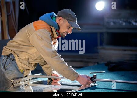 Ein Arbeiter in einer Möbelindustrie schneidet einen Spiegel mit einem Glasschneider. Stockfoto