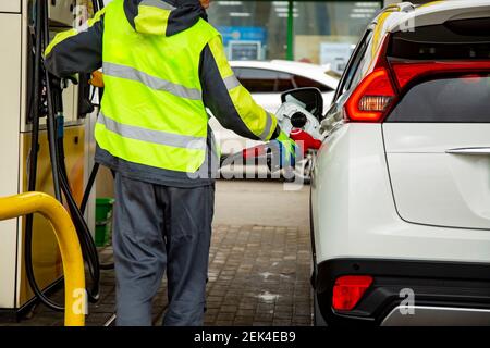Tankstellenmitarbeiter in Overalls tanken das Auto mit Benzin Nahaufnahme. Kein Gesicht Stockfoto