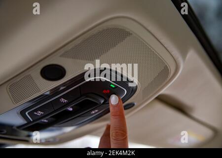 Die Fahrerknopf-Fingerkuppe drückt die sos-Taste an der Deckenplatte Eines modernen Autos Stockfoto