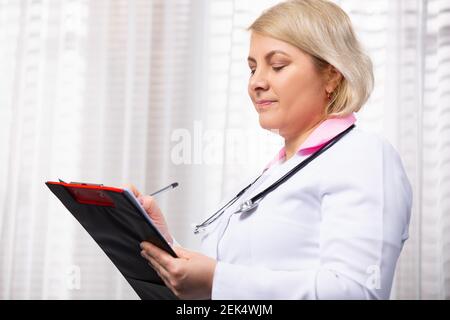 Konzept der medizinischen Dienstleistungen. Porträt von lächelnden weiblichen Arzt schriftlich in Papier Zwischenablage, die Patienten Geschichte und lächeln süß, weiß medizinische Stockfoto
