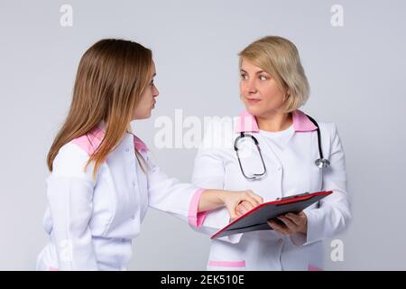 Erstaunt, schockiert, schwindelerregende Ärzte diskutieren Diagnose während der Konferenz in Blatt Ordner zeigen. Erfolgreiche Mitarbeiter im Gesundheitswesen auf grau Stockfoto