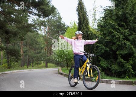 Schöne lächelnde Teenager-Mädchen in Sport-Uniform, Fahrrad Helm, Arme ausgestreckt, Fahrten gelb Fahrrad vor dem Hintergrund des Pinienwaldes. Bike Ride Stockfoto