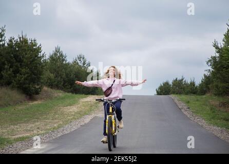 Cute glücklich Teenager-Mädchen mit ausgestreckten Armen, nicht das Lenkrad halten, radelt die Straße hinunter. Harmonie, Freiheit, Gefühle der Freude, Energie o Stockfoto