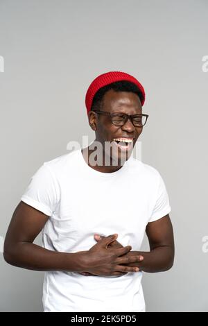 Überglücklich zeigt Black Millennial Mann ihr breites Lächeln, hält seinen Magen vor Lachen. Studio. Stockfoto