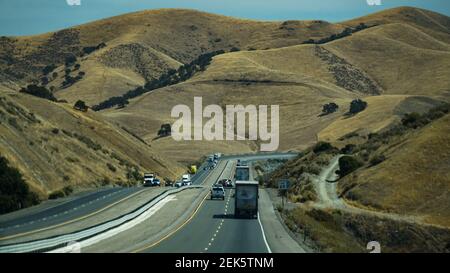 Fahrzeuge fahren durch die Nachmittagssonne in einer hügeligen Landschaft in Kalifornien, USA Stockfoto