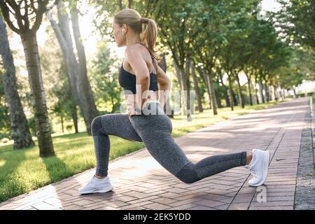 Fühlen Sie sich fit. Sportliche Frau mittleren Alters in Sportbekleidung suchen konzentriert, Stretching ihre Beine beim Training in einem grünen Park an einem sonnigen Tag Stockfoto