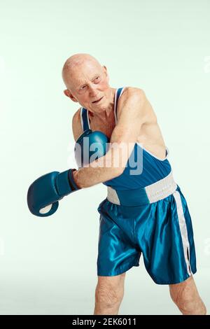 Tritt. Senior Mann trägt Sportbekleidung Boxen auf Studio Hintergrund. Kaukasisches männliches Modell in guter Form bleibt aktiv und sportlich. Konzept von Sport, Aktivität, Bewegung, Wohlbefinden. Copyspace, Anzeige. Stockfoto