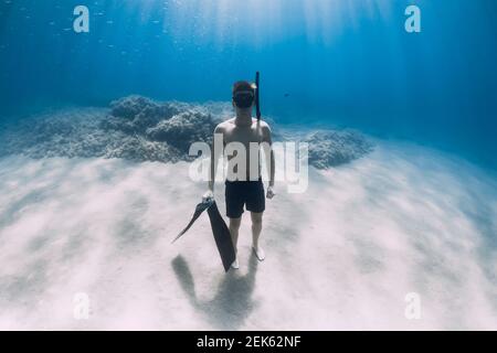 Sportlicher Mann Freediver Aufenthalt mit Flossen auf sandigen Boden unter Wasser im tropischen Meer. Stockfoto