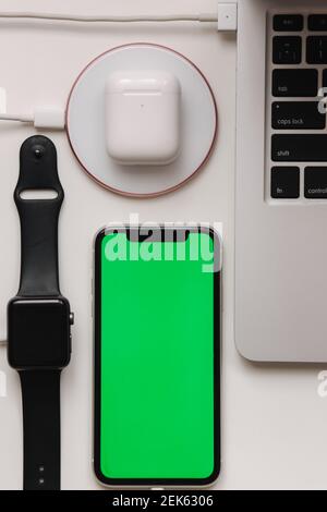 Aufladen verschiedener Geräte am Arbeitsplatz. Wenige Kabel für kabelloses Laden. Laptop, Smart Watch, Smartphone mit grünem Bildschirm und ohne Wissen Stockfoto