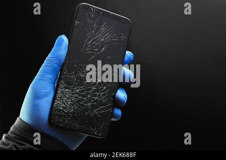 Ein defektes Touch-Telefon mit einem rissigen Bildschirm in der Hand auf schwarzem Hintergrund. Stockfoto
