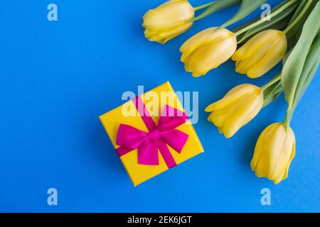 Geschenk mit rosa Schleife und gelben Tulpen auf dem blauen Hintergrund. Draufsicht. Speicherplatz kopieren. Stockfoto