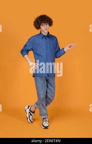 Zeigt zur Seite. Kaukasischen gut aussehenden jungen Mann Porträt isoliert auf gelben Studio-Hintergrund mit Copyspace. Männliches Modell mit lockigen Haaren. Konzept der menschlichen Emotionen, Gesichtsausdruck, Verkauf, Werbung, Mode. Stockfoto