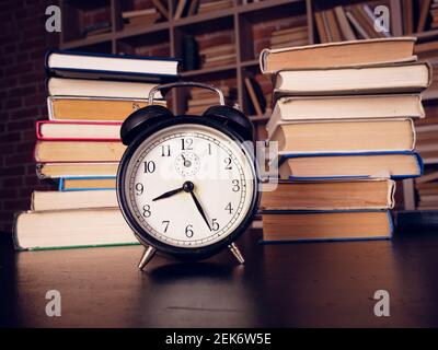 Zeit für das Lernkonzept. Wecker und viele Bücher in der Bibliothek. Stockfoto