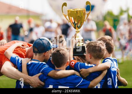 Boys Sport Team feiert Erfolg mit jungen Trainer. Teamkapitän steigt goldene Trophäe mit Teamkollegen. Glück in der Schulfußballmannschaft nach dem Winnin Stockfoto