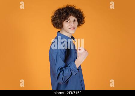 Zeigen. Kaukasischen gut aussehenden jungen Mann Porträt isoliert auf gelben Studio-Hintergrund mit Copyspace. Männliches Modell mit lockigen Haaren. Konzept der menschlichen Emotionen, Gesichtsausdruck, Verkauf, Werbung, Mode. Stockfoto