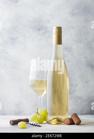 Glas und Flasche Sommer Weißwein mit Trauben, Korken und Korkenzieher auf hellem Stein Hintergrund. Stockfoto