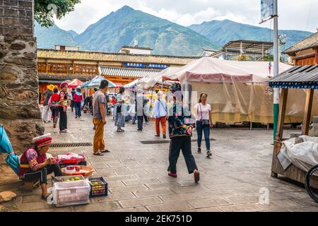 Dali China , 6. Oktober 2020 : Zhoucheng Dorf Marktplatz Ansicht mit Bai Minderheit Menschen in traditioneller Kleidung und Cangshan Berg im Hintergrund Stockfoto