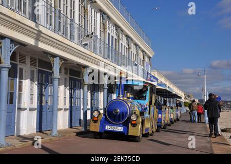 Der Landzug in Weymouth fährt entlang der Promenade vor den viktorianischen Umkleidekabinen. Stockfoto