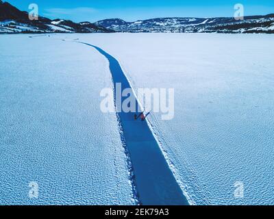 Eisläufer ruhen auf einem großen gefrorenen See mit klarem glasigen und rissigen Eis. Stockfoto