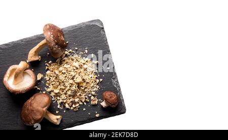 Flache Ansicht von trockenem Pulver aus Shiitake-Pilzen, Lentinula edodes. Lebensmittelzutat auf Schneidebrett aus schwarzem Stein mit frischen Shiitake-Pilzen i Stockfoto