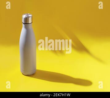 Nahaufnahme der grauen wiederverwendbaren Stahlflasche auf gelbem Hintergrund mit Hartes Licht Stockfoto