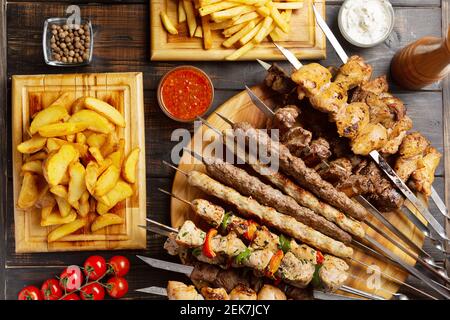 Gericht aus Spieße, gegrilltes Huhn, Rindfleisch, Schweinefleisch mit bbq und Tzatziki-Sauce mit Pommes Frites auf dunklem Hintergrund serviert. Stockfoto