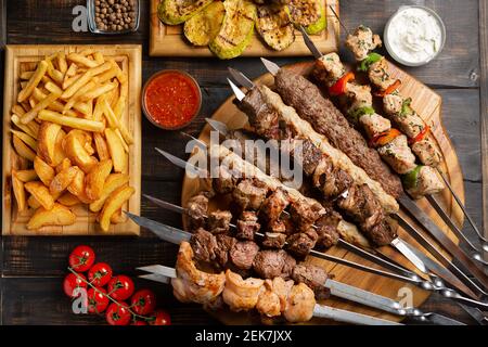 Gericht aus Spieße, gegrilltes Huhn, Rindfleisch, Schweinefleisch mit bbq und Tzatziki-Sauce mit Pommes Frites auf dunklem Hintergrund serviert. Stockfoto