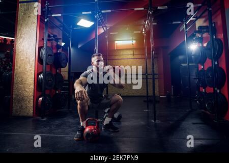 Fokussierte starke Bodybuilder dabei hockt mit Gewichten im Fitnessstudio. Stockfoto