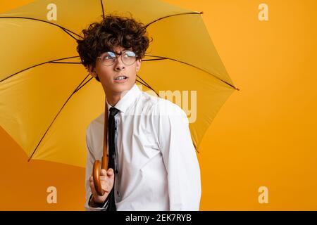 Selbstbewusster junger Mann mit weißem Hemd und Krawatte Regenschirm isoliert auf gelbem Hintergrund Stockfoto