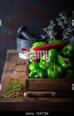 Zubereitung der Speisen mit frischem grünen Paprika. Frischer grüner Paprika und roter Pfeffer mit Zwiebel, Knoblauch und Gewürzen auf natürlichem Holzhintergrund. Stockfoto