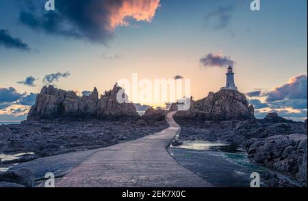 Straße zu La Corbiere Leuchtturm auf dem Meeresgrund bei Ebbe mit Klippe und Sonnenuntergang, Vogtei von Jersey, Kanalinseln Stockfoto