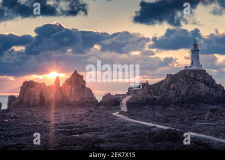 Straße zu La Corbiere Leuchtturm auf dem Meeresgrund bei Ebbe mit Klippe und Sonnenuntergang, Vogtei von Jersey, Kanalinseln Stockfoto