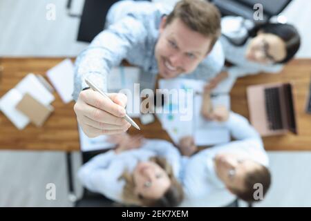 Eine Gruppe von Geschäftsleuten sitzt am Tisch von oben. Mann zeigt den Stift nach oben Stockfoto