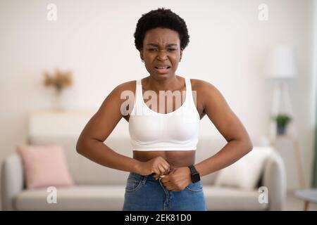 Frustriert Schwarz Frau Knöpfend Kleine Jeans Nach Gewichtszunahme Im Innen Stockfoto