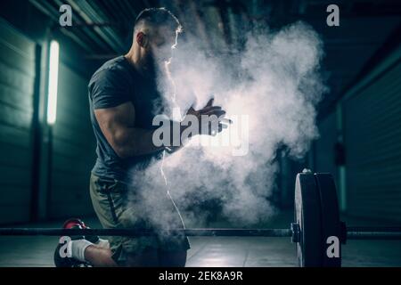 Seitenansicht muskulöser attraktiver kaukasischer bärtiger Mann kniet und käufelt seine Hände. Stockfoto