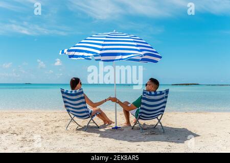 Ein glückliches Paar sitzt auf Stühlen unter dem Sonnenschirm an einem tropischen Strand. Sommerurlaub Konzept. Stockfoto