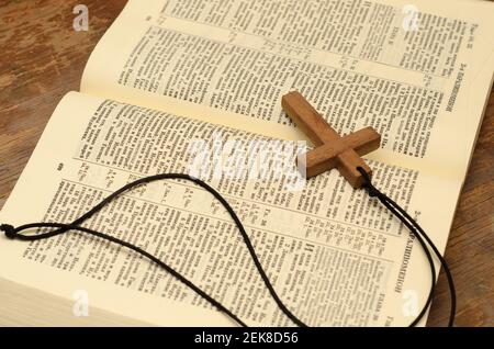 Hölzernes christliches Kreuz mit Seil auf offener Heiliger bibel. Stockfoto