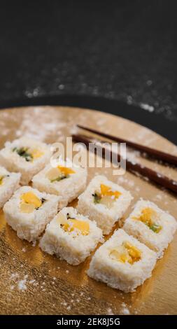 Sushi-Lieferung. Süße Brötchen aus Reis, Ananas, Kiwi und Mango. Rollt auf einem goldenen und schwarzen Hintergrund. Holzstöcke für Sushi. Stockfoto