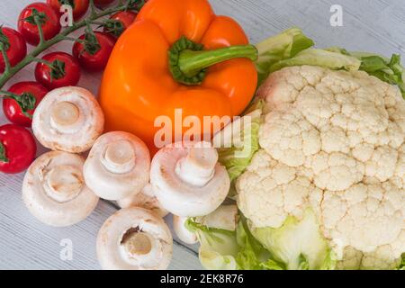 Tomaten, Pilze, Orangenpfeffer und Blumenkohl auf einem weiß bemalten Brett aus dem Wintergarten. Stockfoto