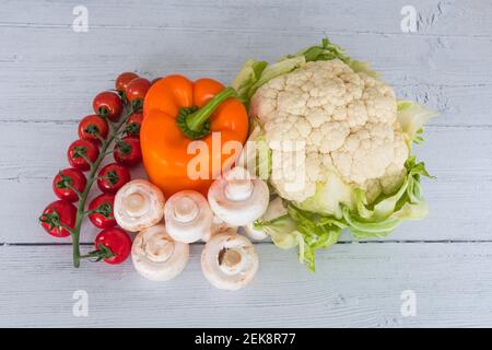 Tomaten, Pilze, Orangenpfeffer und Blumenkohl auf einem weiß bemalten Brett aus dem Wintergarten. Stockfoto