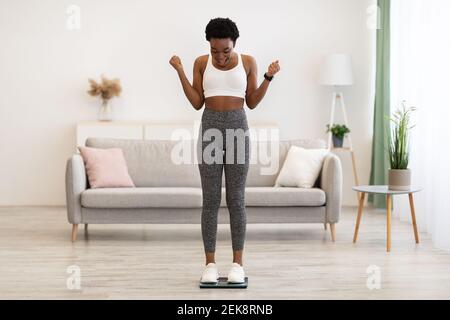 Aufgeregt Afrikanische Frau Auf Waage Schütteln Fäuste Nach Slimming Indoors Stockfoto