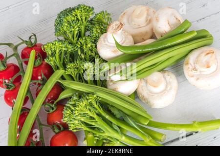 Tenderstem Broccoli, Tomaten, grüne Bohnen und Pilze auf einem weiß bemalten Brett aus dem Wintergarten ausgelegt. Stockfoto