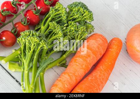 Tenderstem Broccoli, Zwiebeln, Tomaten und Karotten auf einem weiß bemalten Brett aus dem Wintergarten ausgelegt. Stockfoto